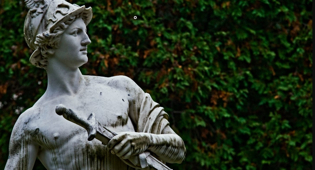 A picture of a statue of the Greek God Hermes. He is looking to his left and holding a sword. 