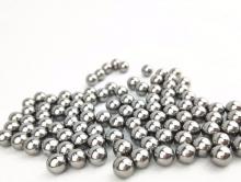 A large number of metal ball bearings sit on a white surface